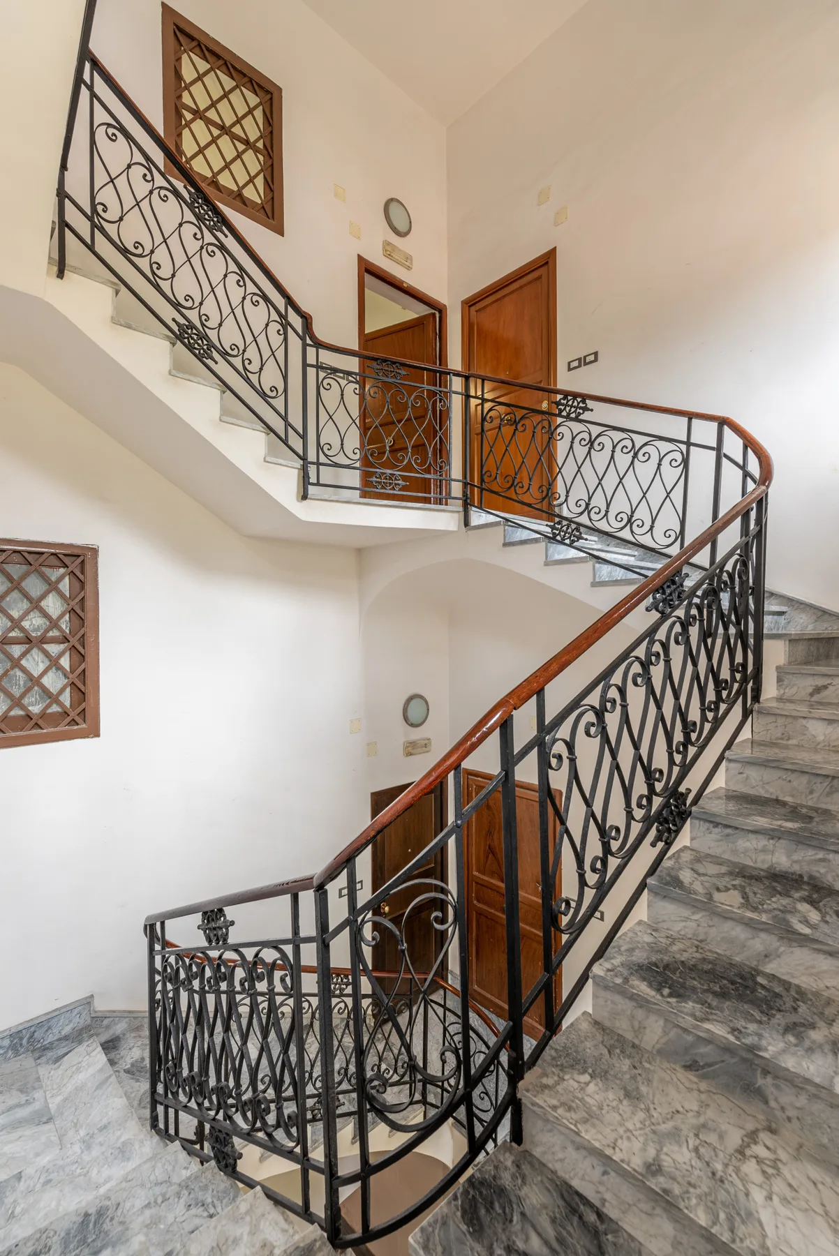 Una escalera interior con barandillas ornamentadas y puertas de madera en el rellano.