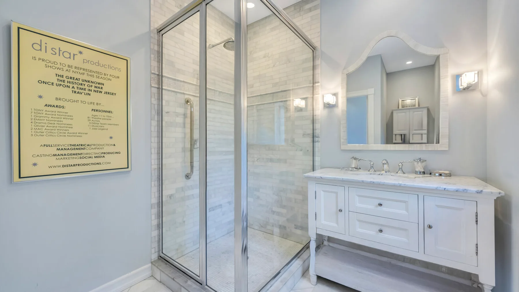 Un baño luminoso tiene una ducha de vidrio junto a un tocador blanco.