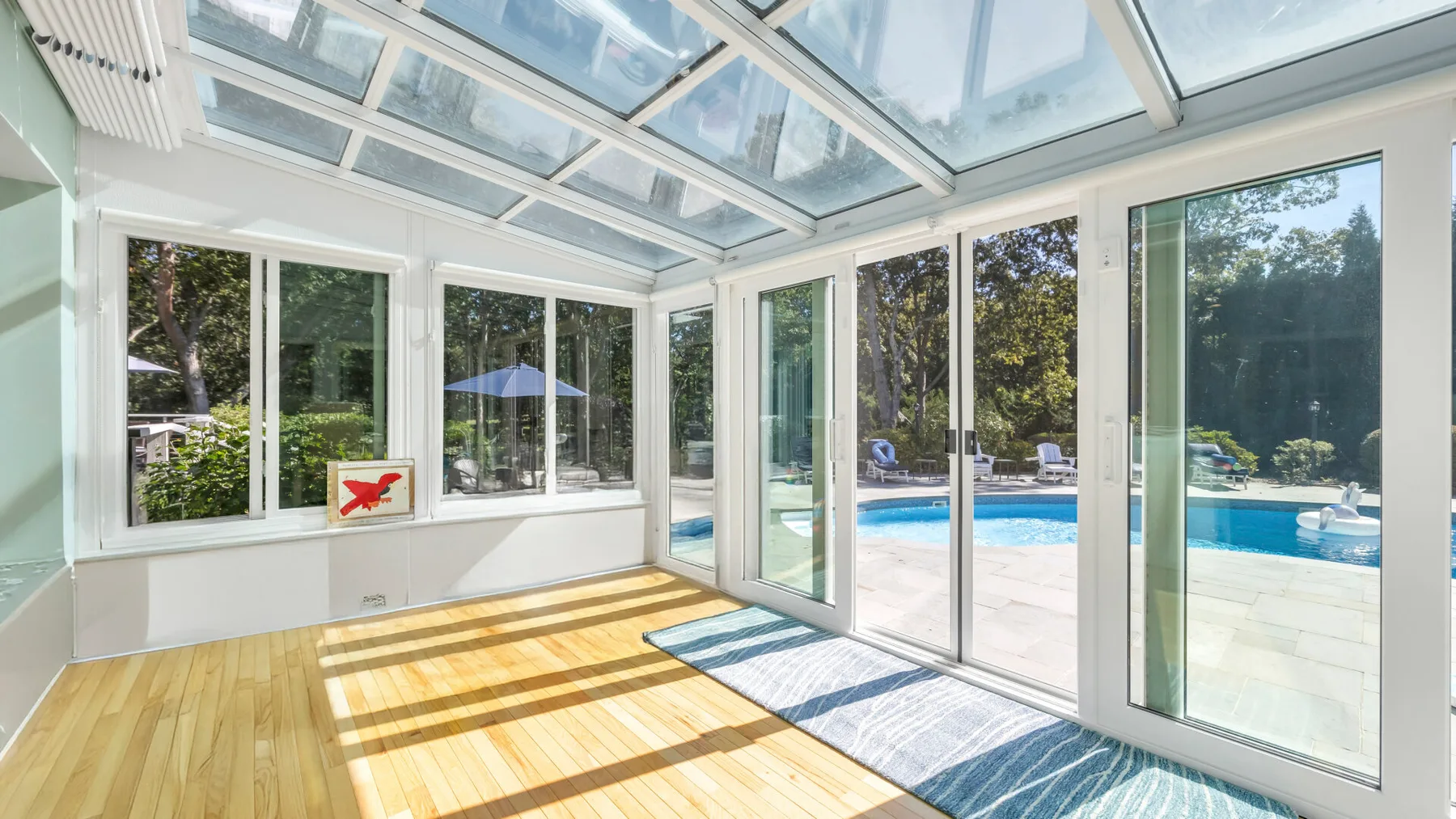 Un solárium luminoso con techo de vidrio y grandes ventanas da a una piscina.