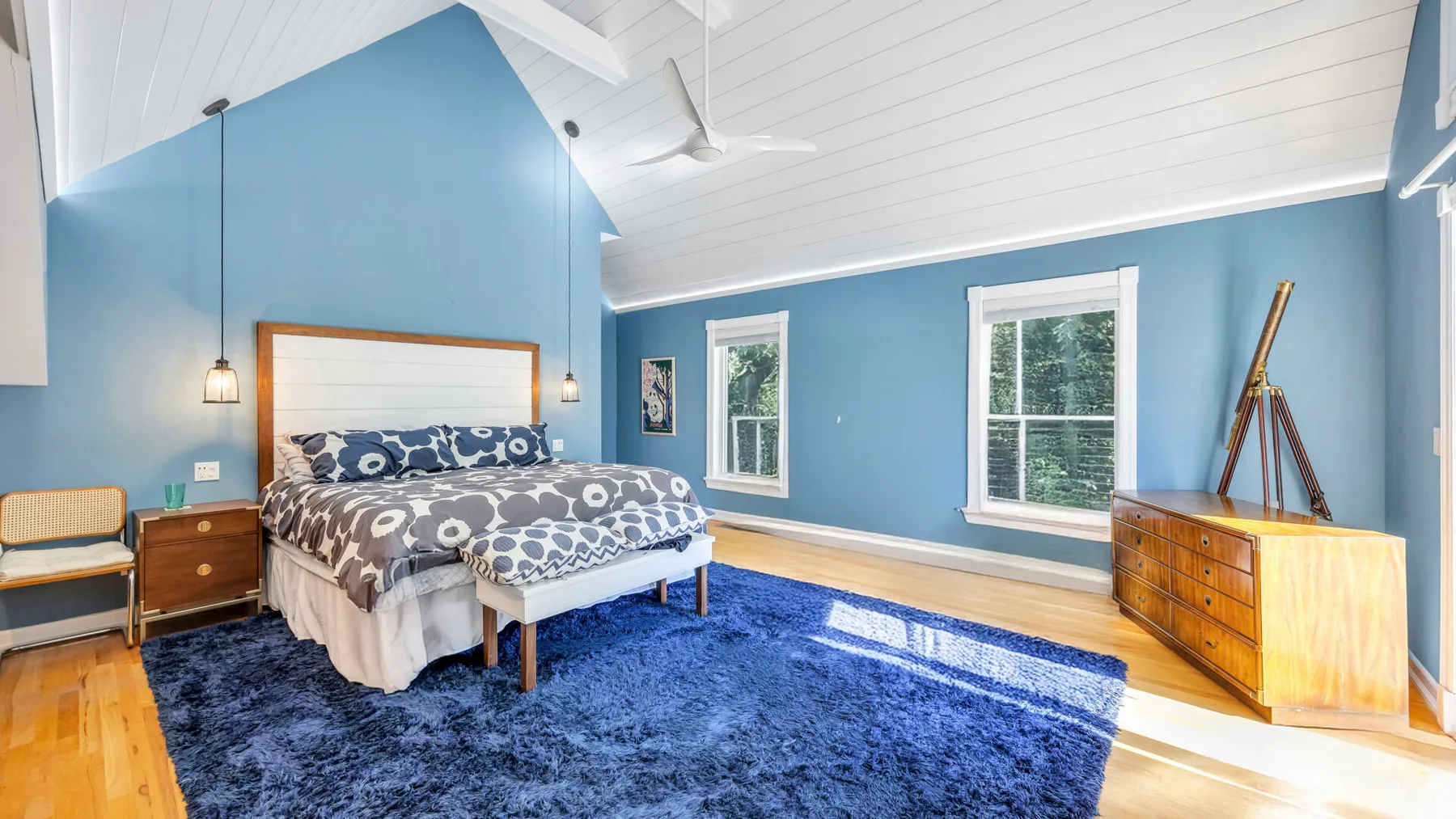 Un dormitorio azul con una cama, ventanas grandes y una alfombra azul.