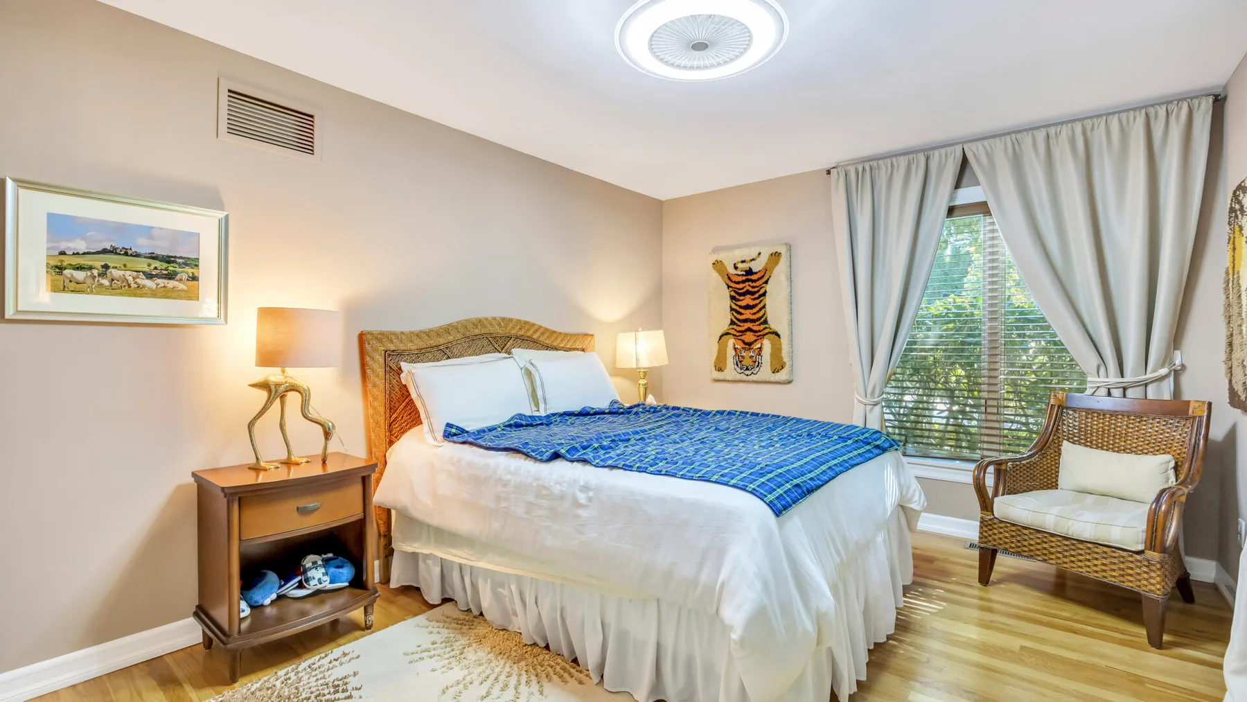 Un dormitorio con una cama tendida, mesas de noche y una ventana con cortinas.