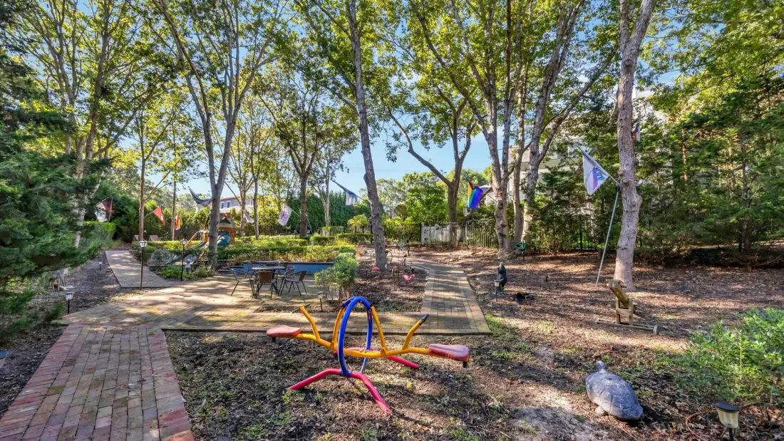 Una zona de juegos al aire libre entre árboles, con un camino pavimentado y juegos coloridos.