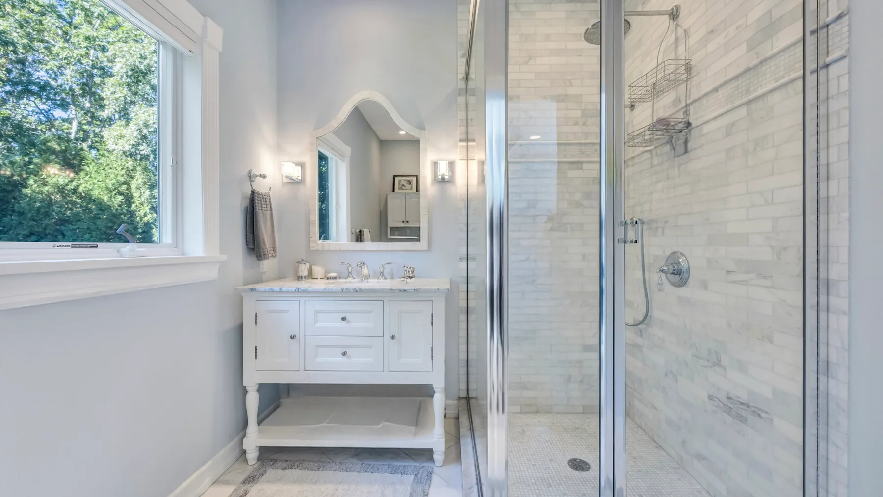 Un baño luminoso con lavabo, espejo y ducha con mampara de vidrio.
