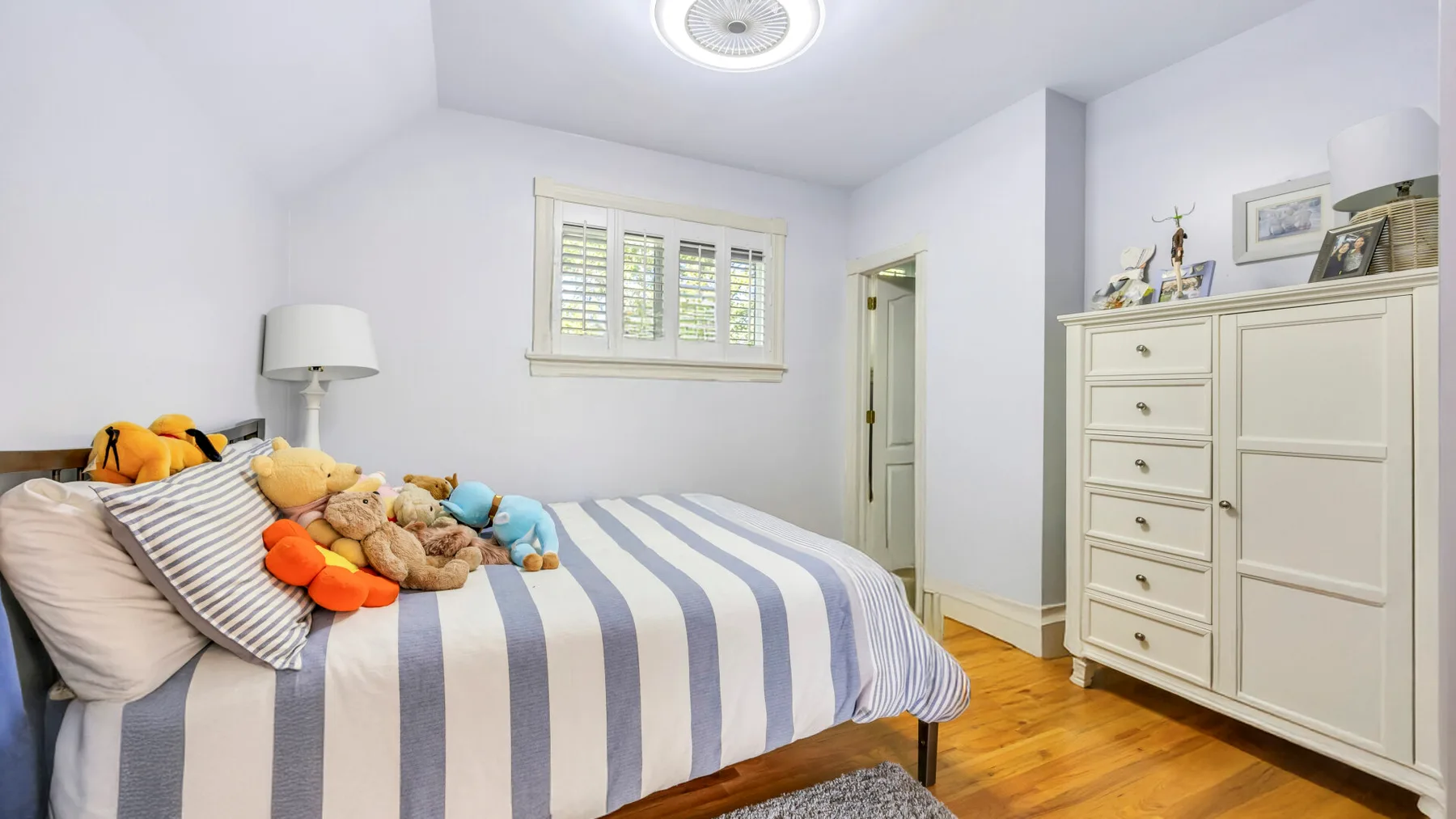 Un dormitorio con una cama a rayas y peluches junto a una ventana.