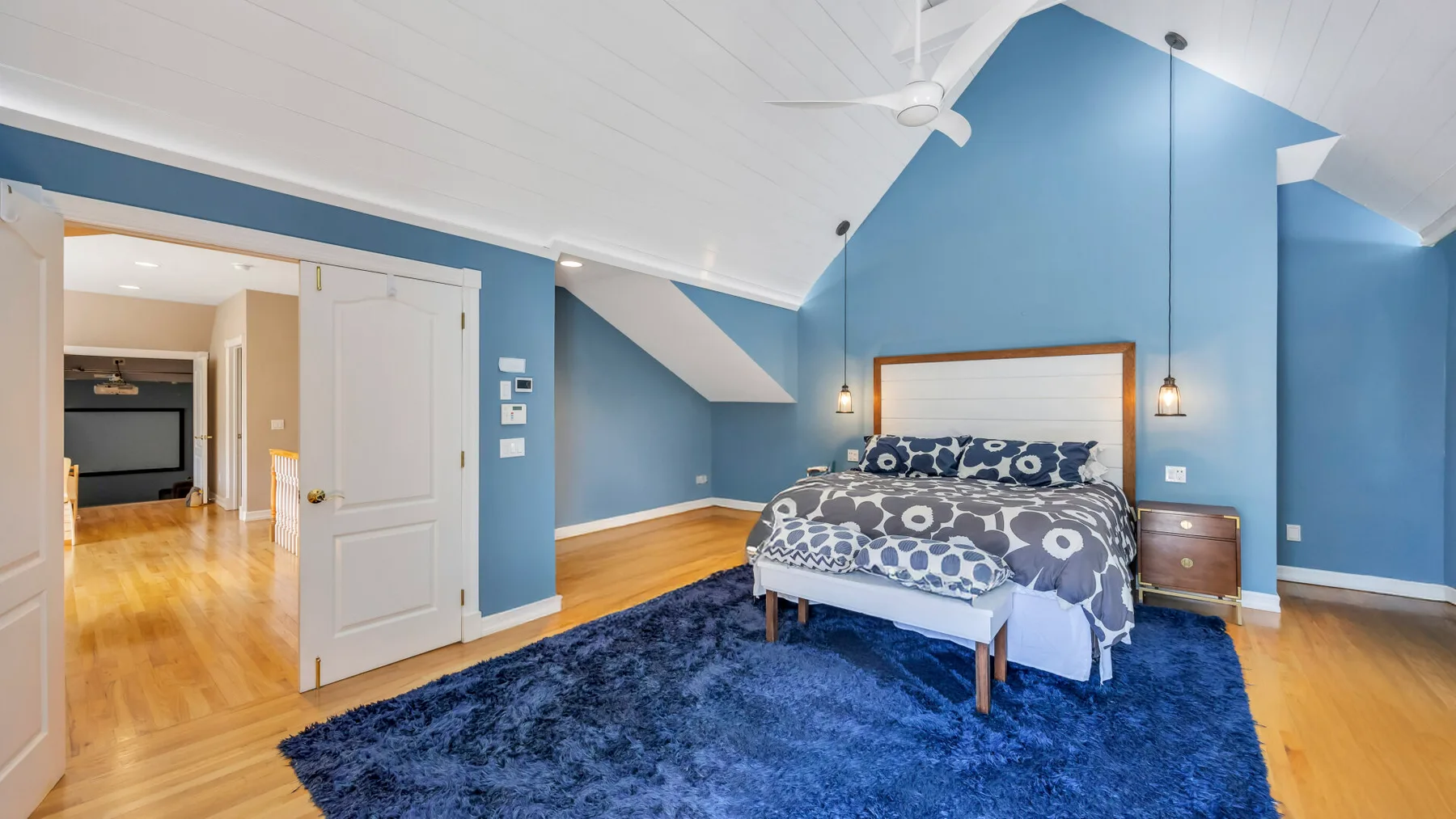 Un dormitorio azul con una cama, mesas de noche y un ventilador de techo.