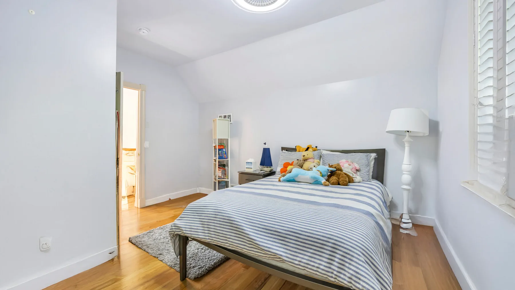 Un dormitorio luminoso con una colcha a rayas y una ventana con persianas.
