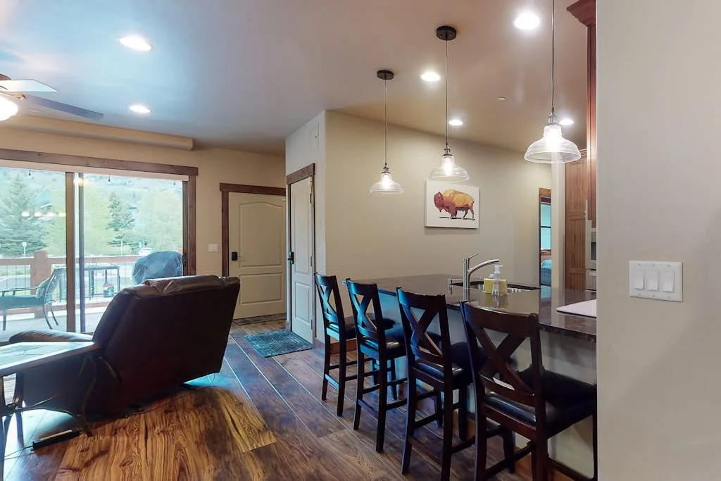 An open dining and living area features a long dining table beside large windows.