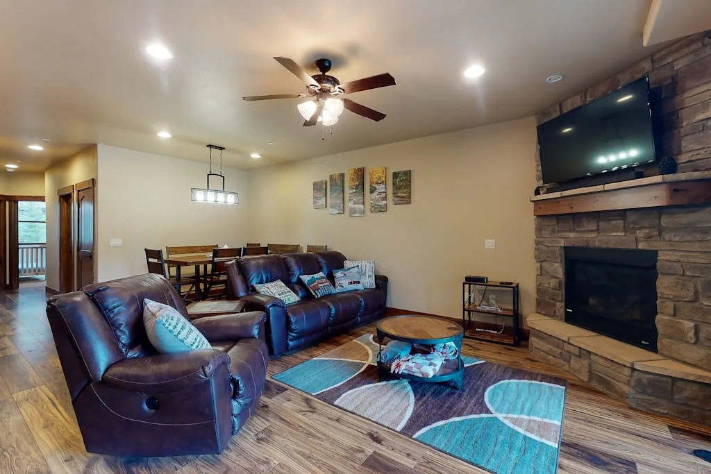 A living room with leather seating, a dining table, and a stone fireplace.