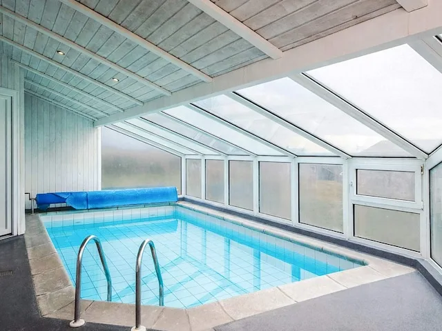 An indoor swimming pool with large windows and a metal ladder.