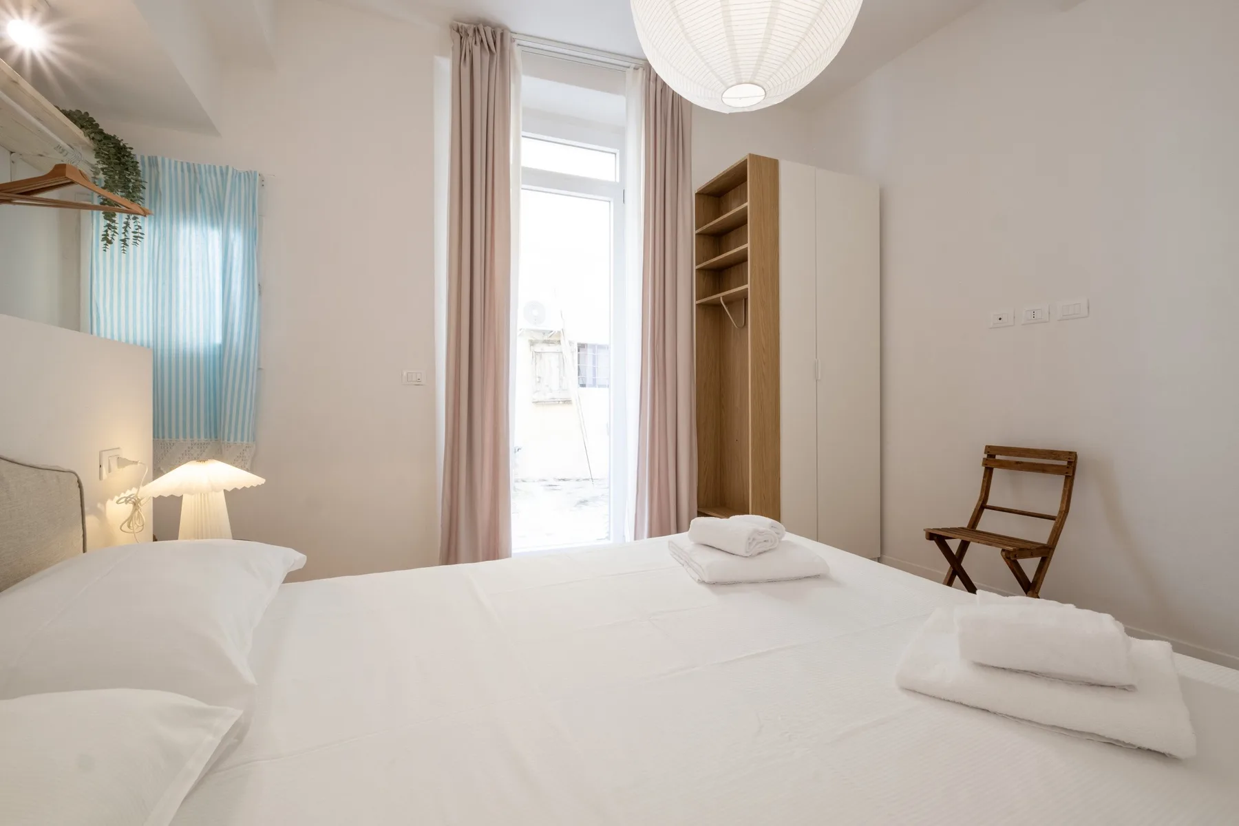 A bright bedroom with a neatly made bed and a small wooden chair.