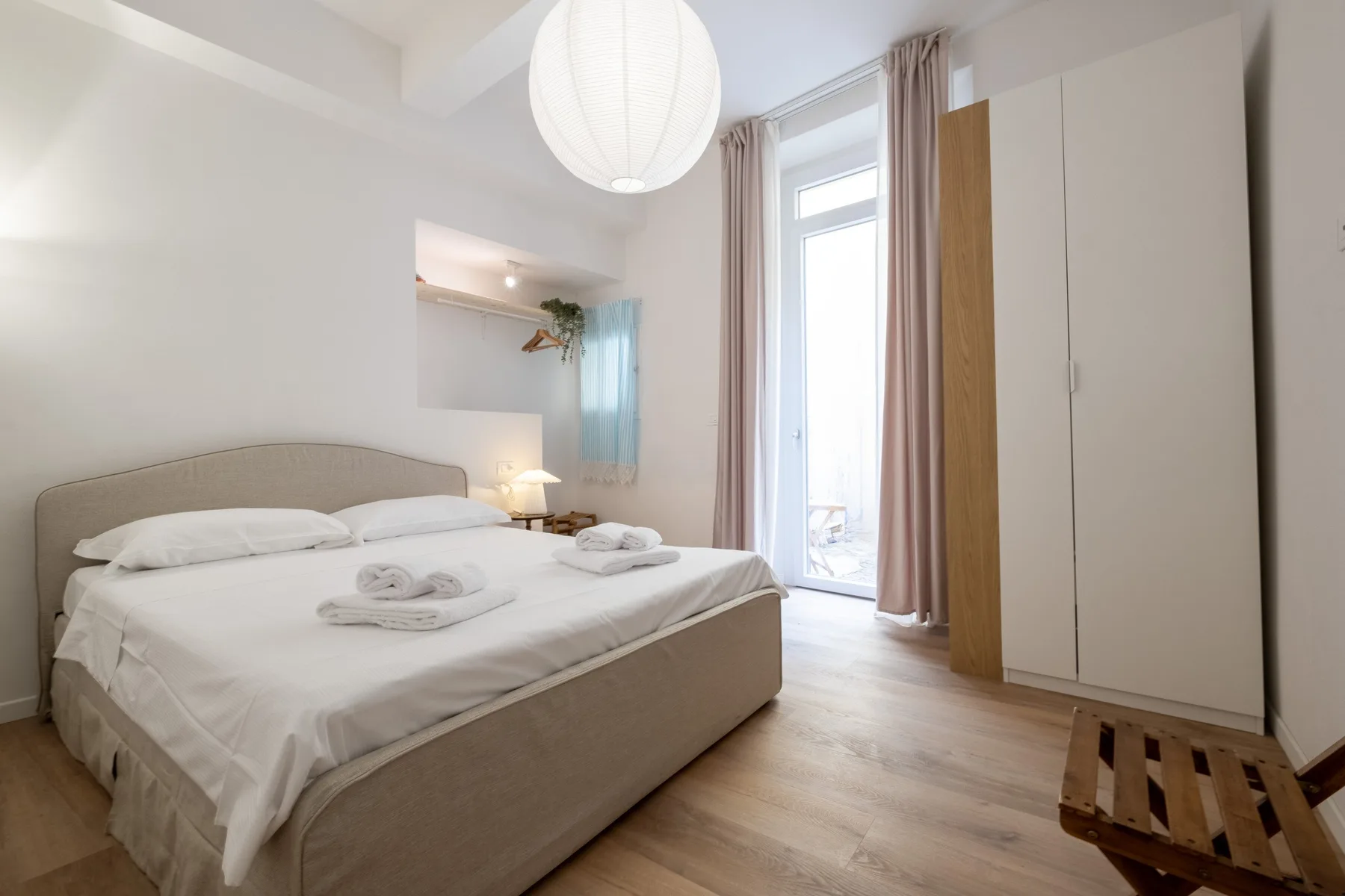 A bright bedroom with a neatly made bed and a tall window.
