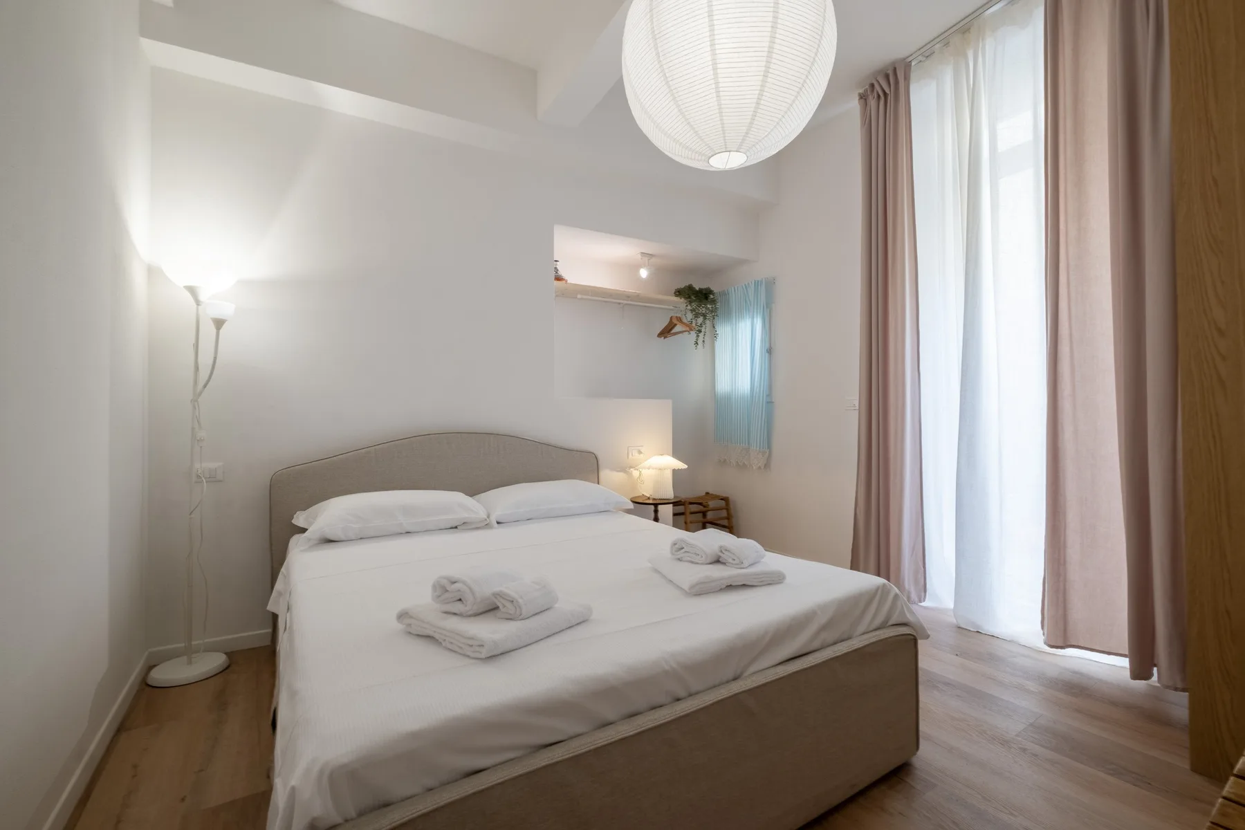 A bedroom with a neatly made bed and tall curtained windows.
