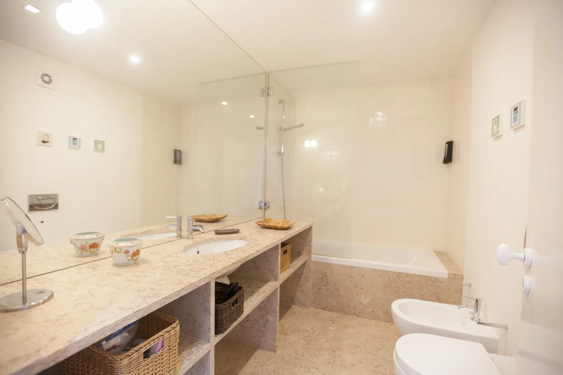 Un baño luminoso con un tocador largo, ducha de vidrio y bañera.