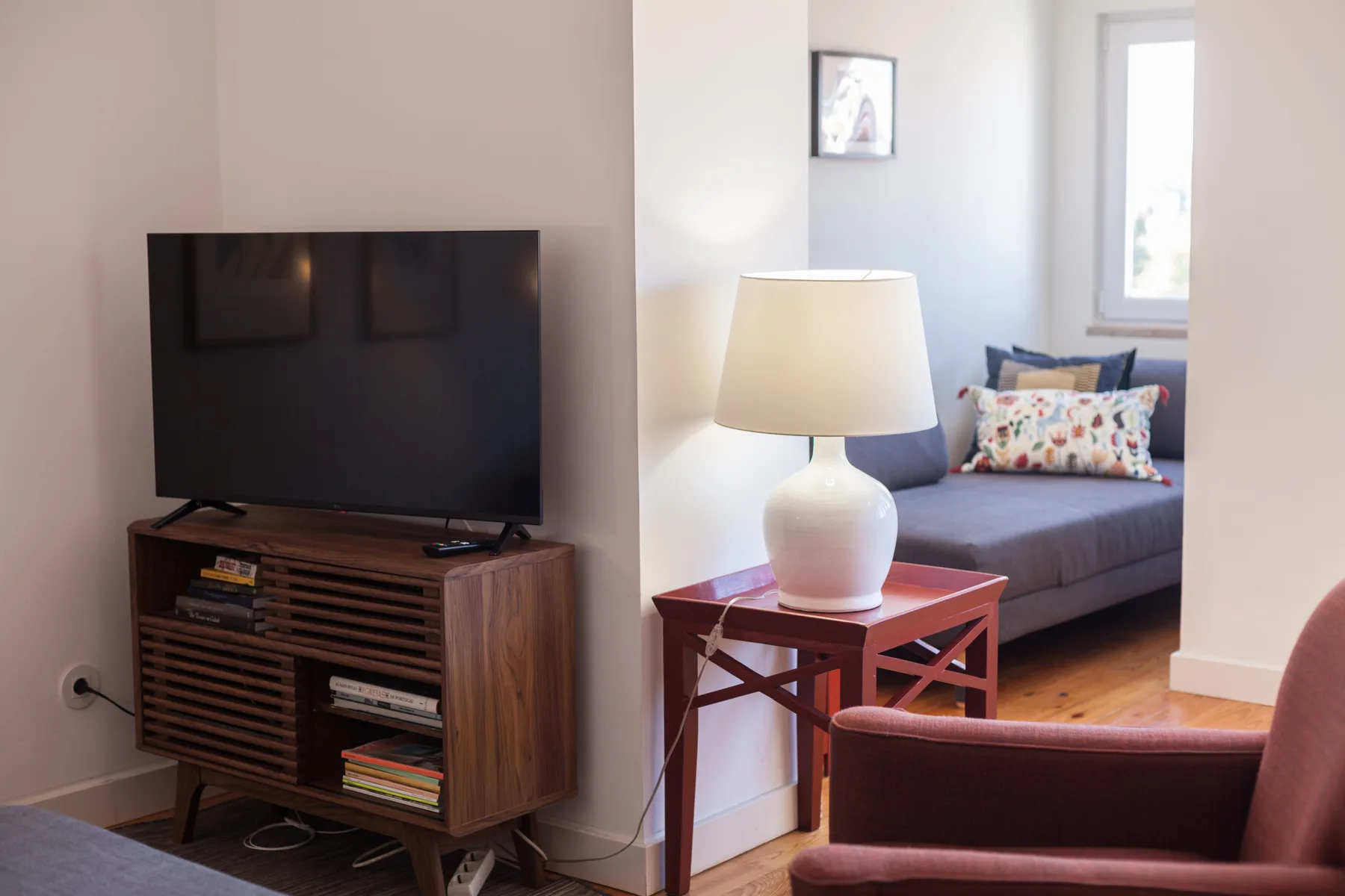 Una sala de estar con televisor, mesa auxiliar y asientos junto a una ventana.
