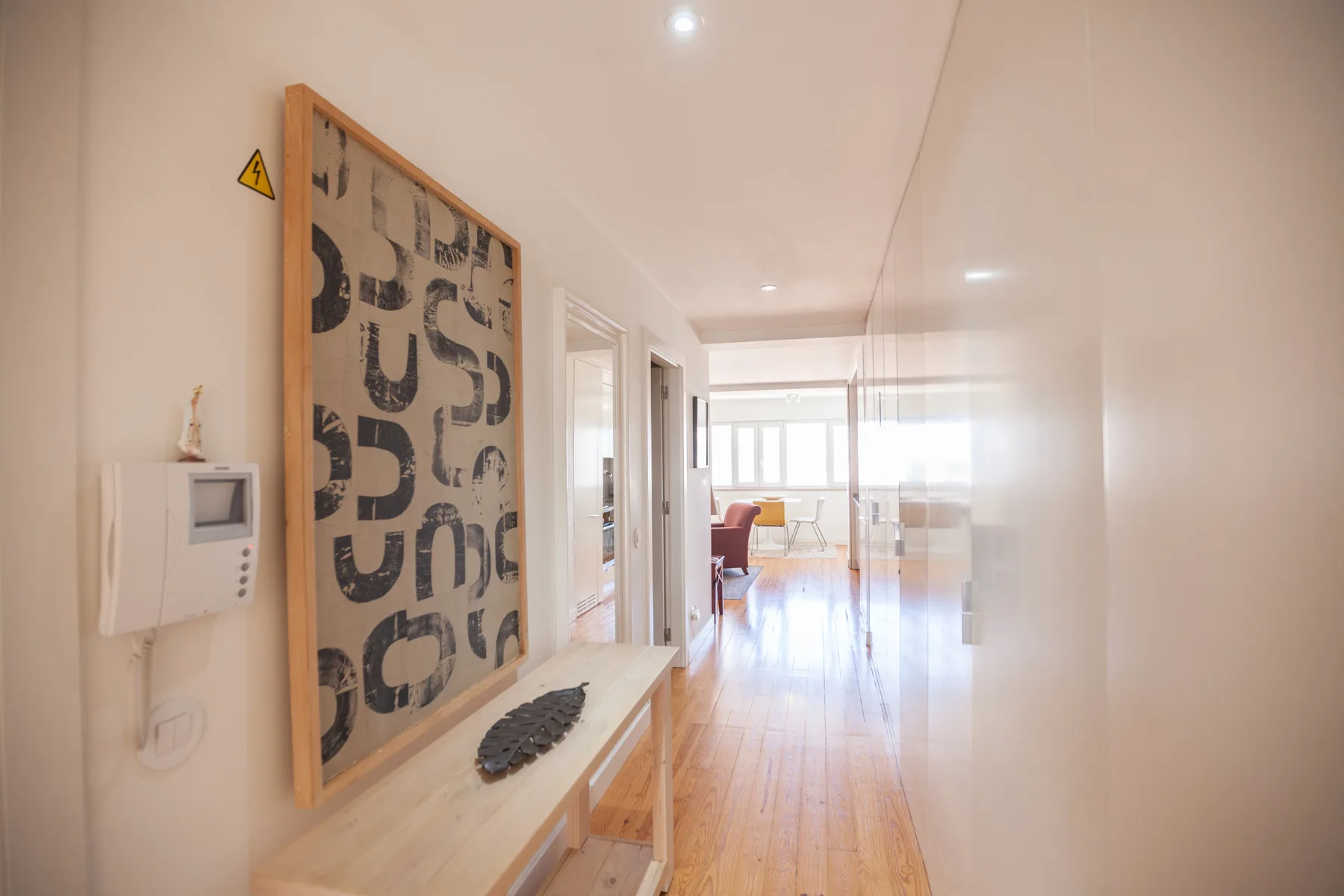 Un pasillo luminoso del apartamento se abre a una sala de estar con grandes ventanas.