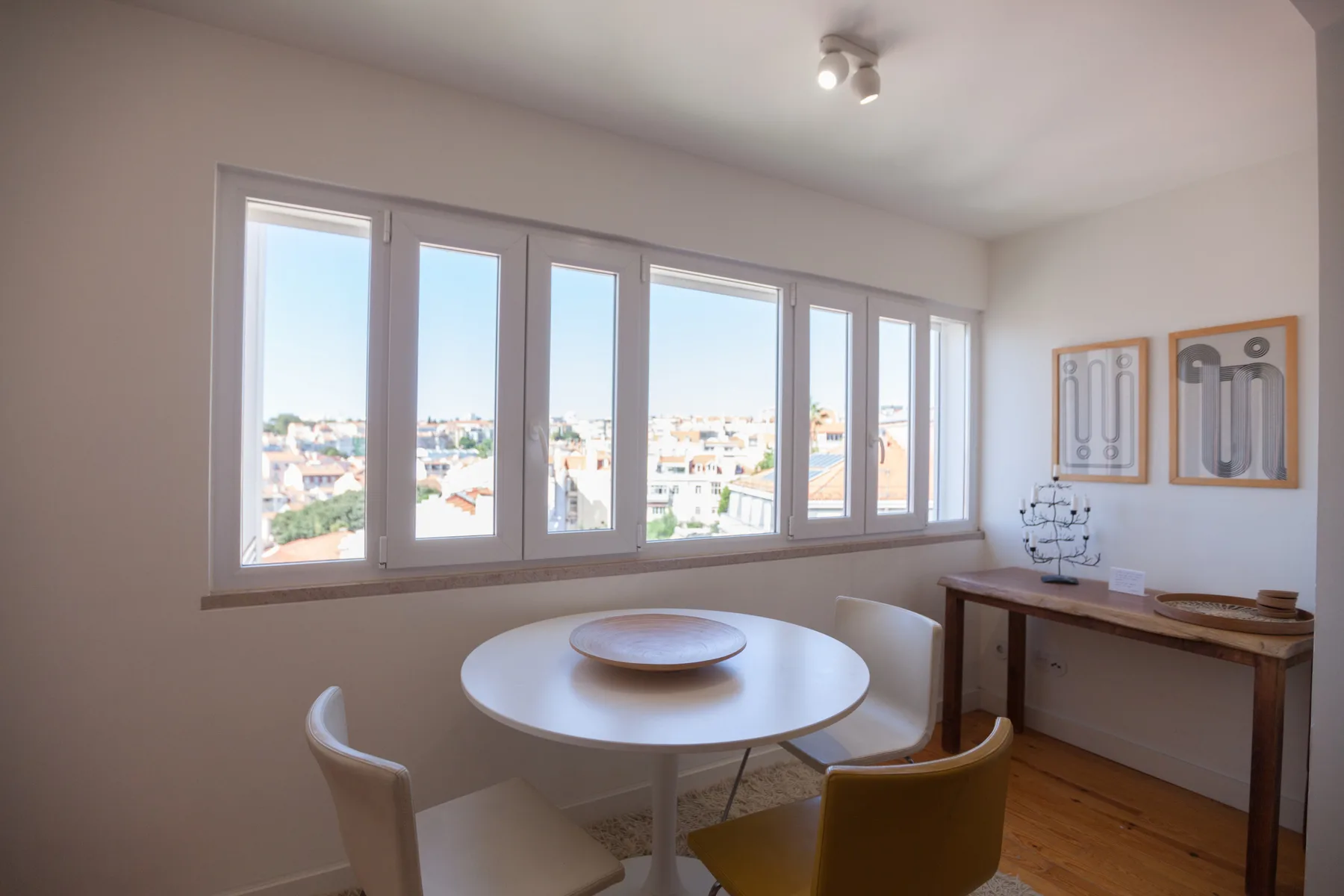 Un comedor luminoso con una mesa redonda junto a una ventana amplia con vistas a los tejados.
