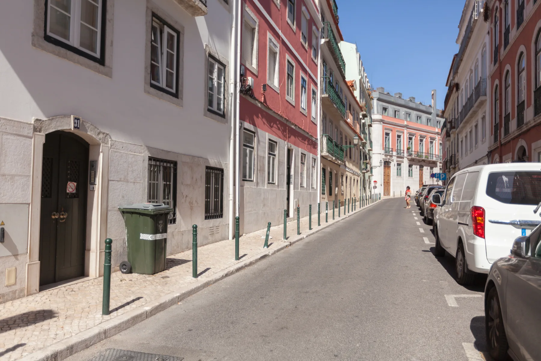 Una calle estrecha bordeada de edificios coloridos y coches aparcados.