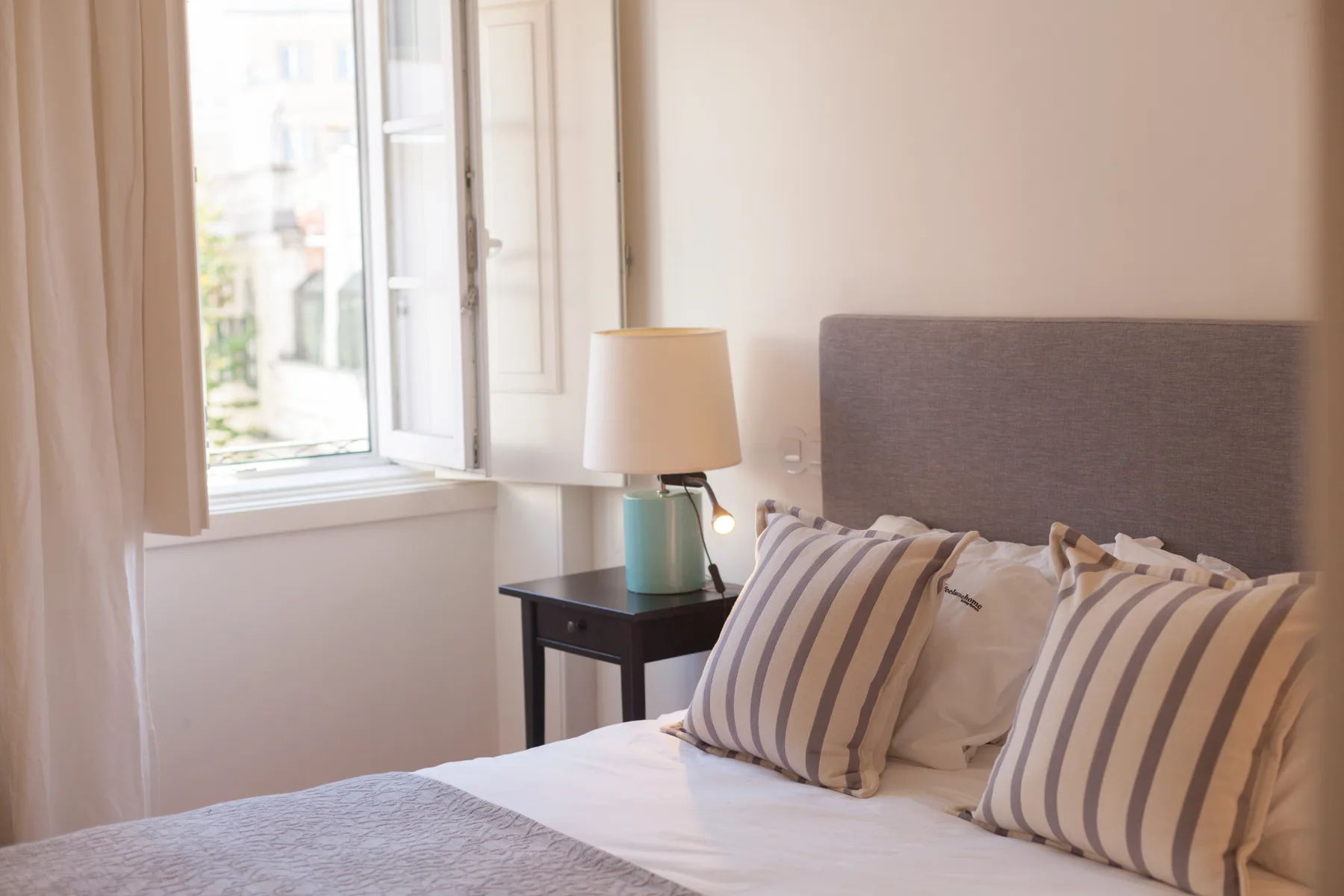 Un dormitorio con cojines a rayas junto a una ventana abierta.
