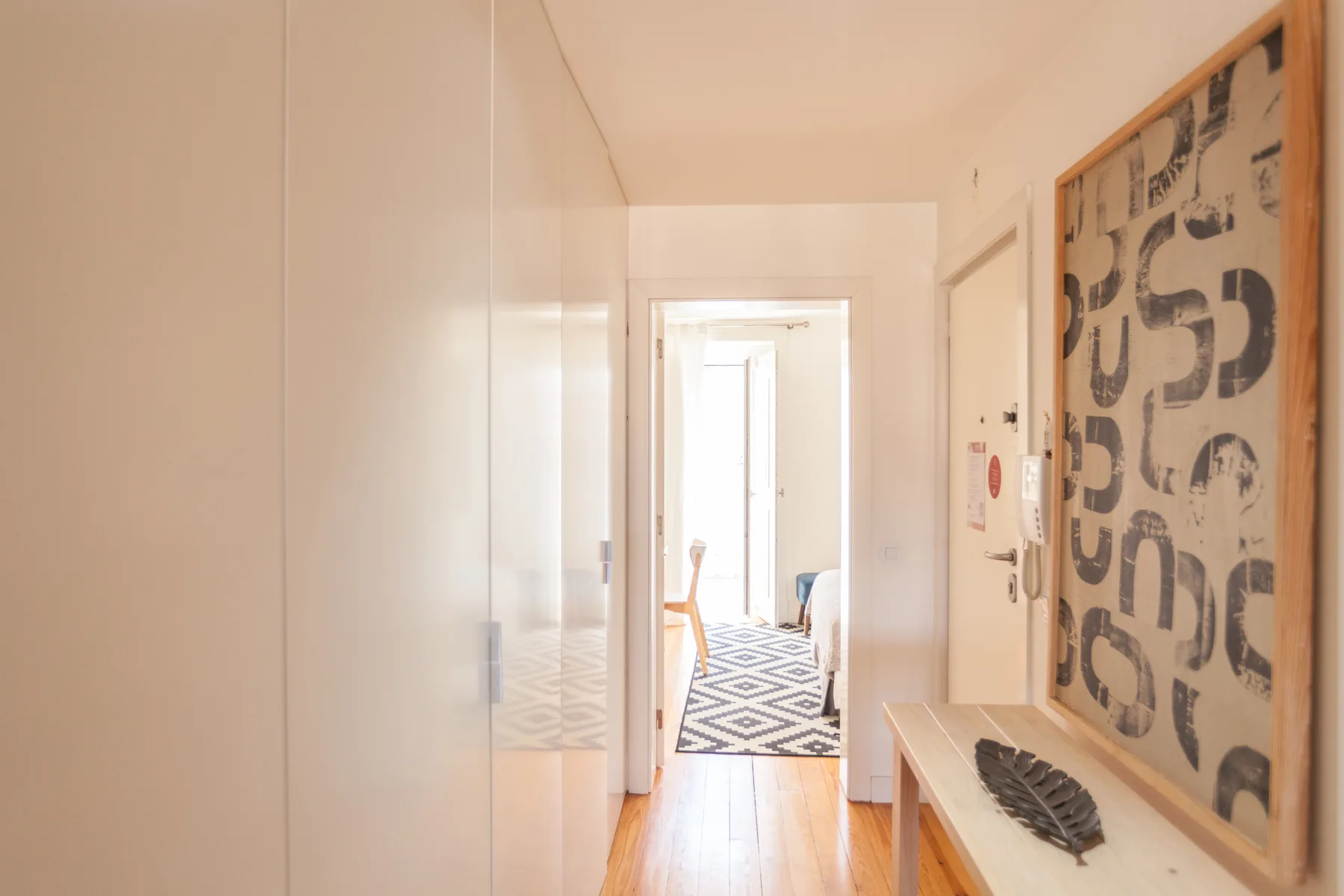 Un pasillo luminoso con una obra estampada y una vista hacia otra habitación.