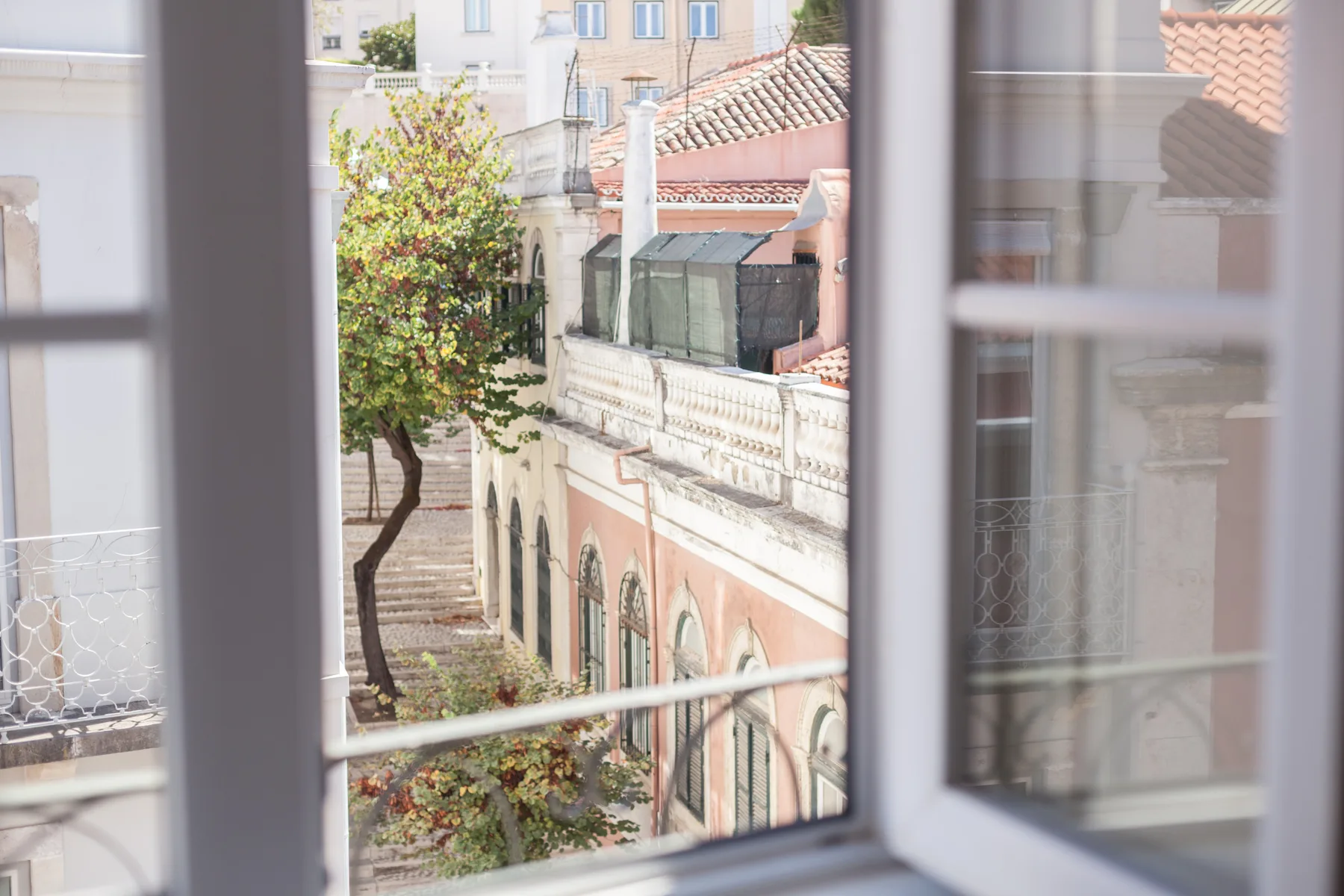 La vista por la ventana muestra edificios cercanos y un árbol.
