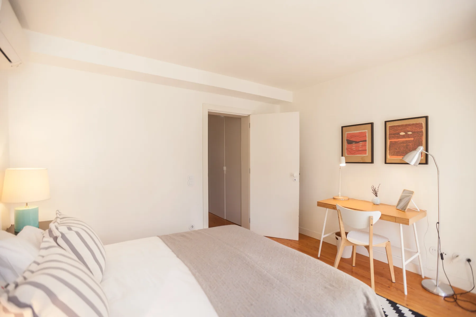 Un dormitorio con una cama y un pequeño escritorio bajo cuadros enmarcados.