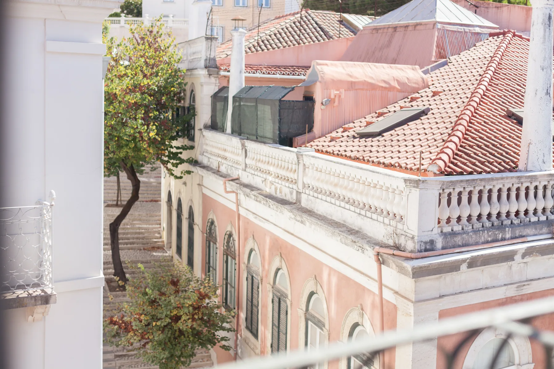 Vista de un edificio rosa con techo de tejas y árboles junto a la calle.