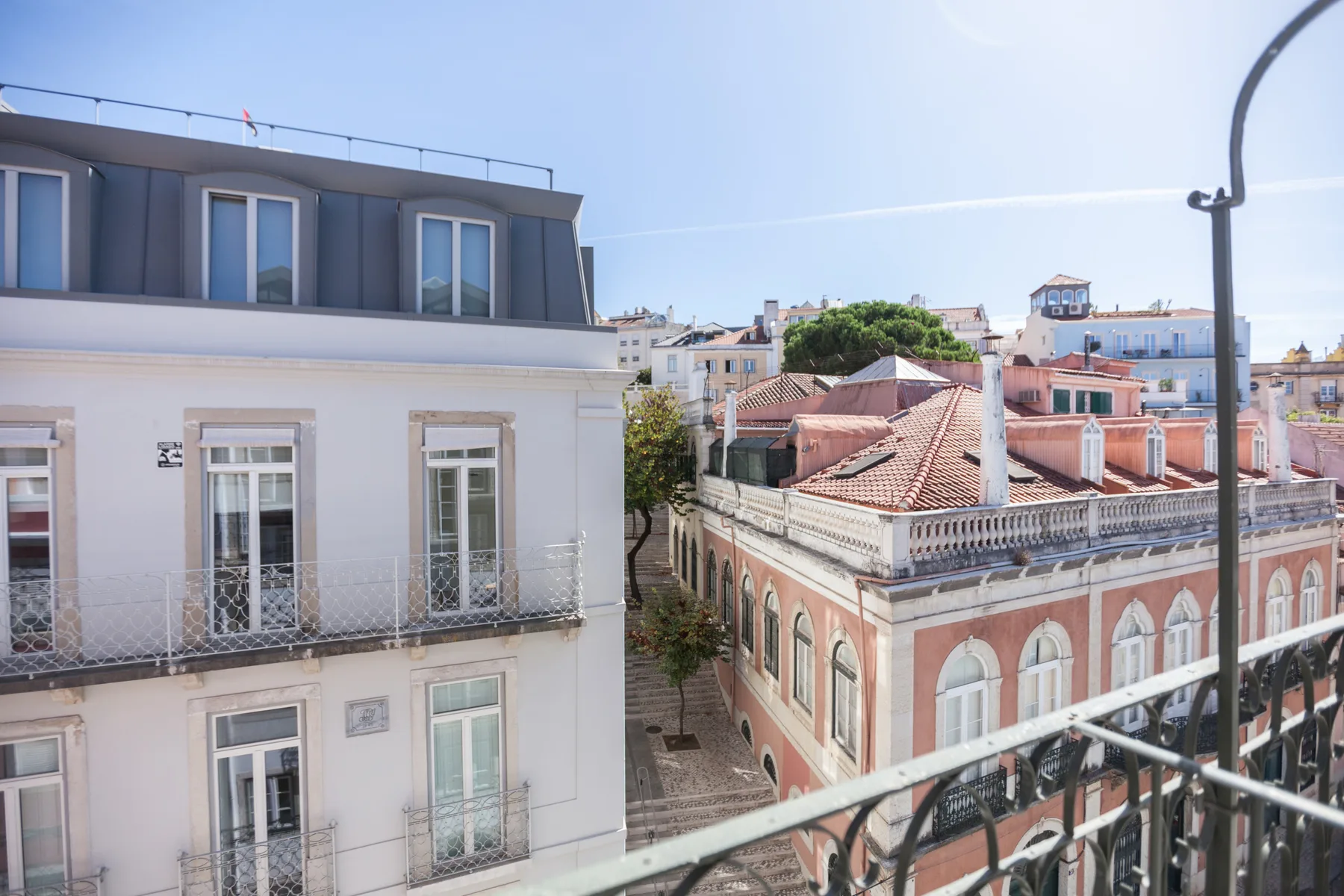 Vista de los tejados de la ciudad desde un balcón, con edificios cercanos y una calle estrecha.