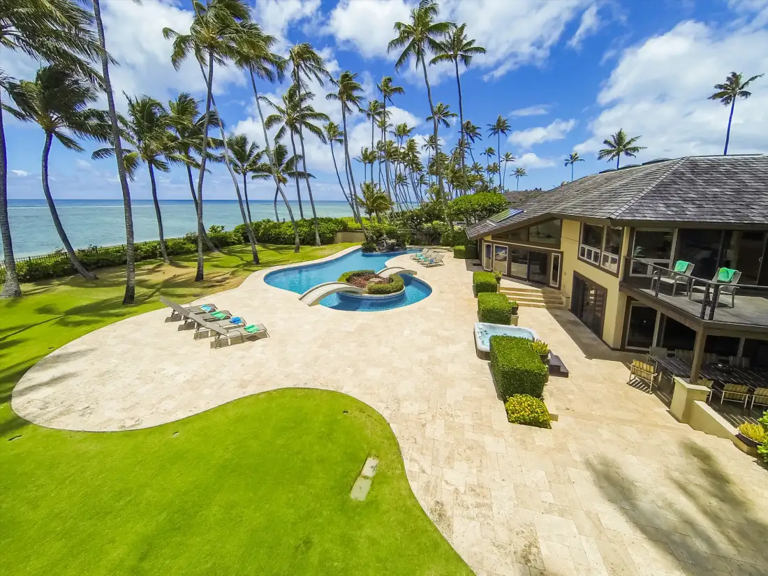 Una propiedad tropical frente al mar con una piscina curva y palmeras.