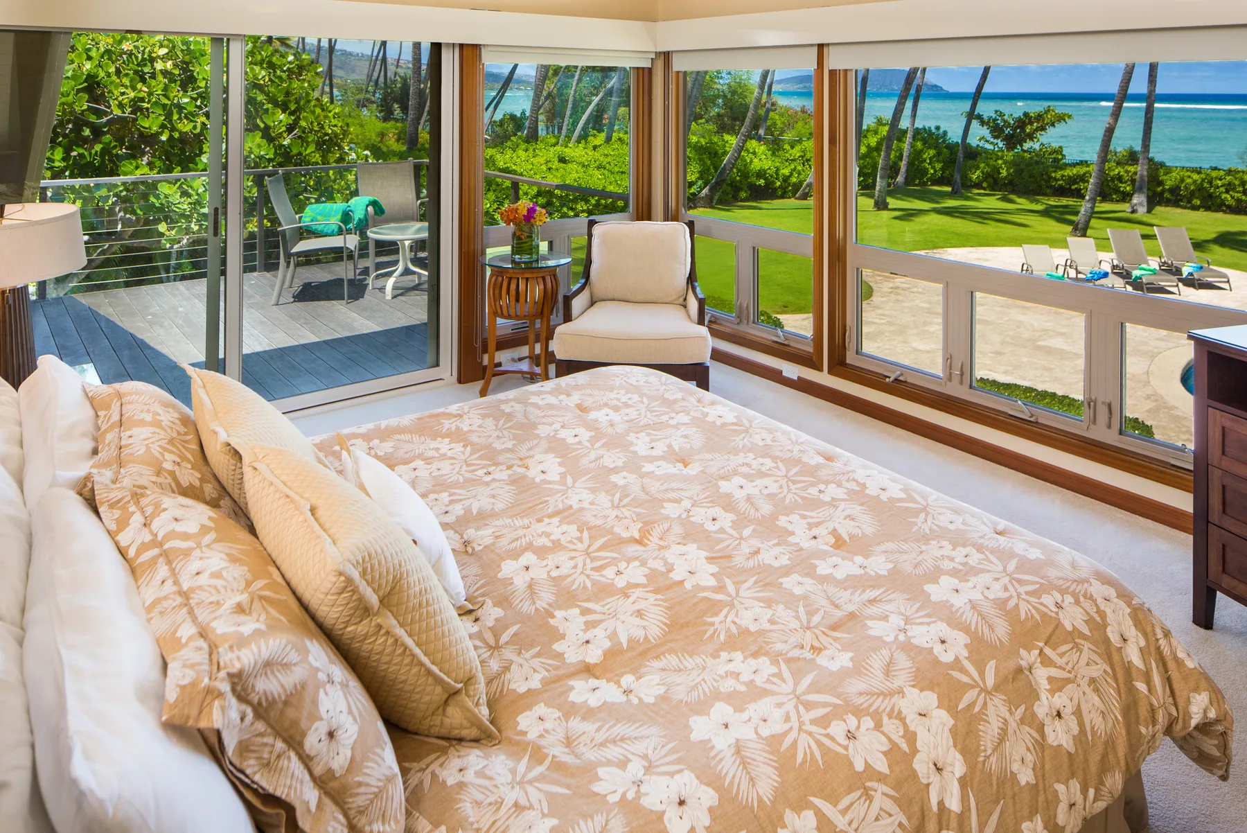 Dormitorio con una colcha floral y amplios ventanales con vistas al jardín y al océano.