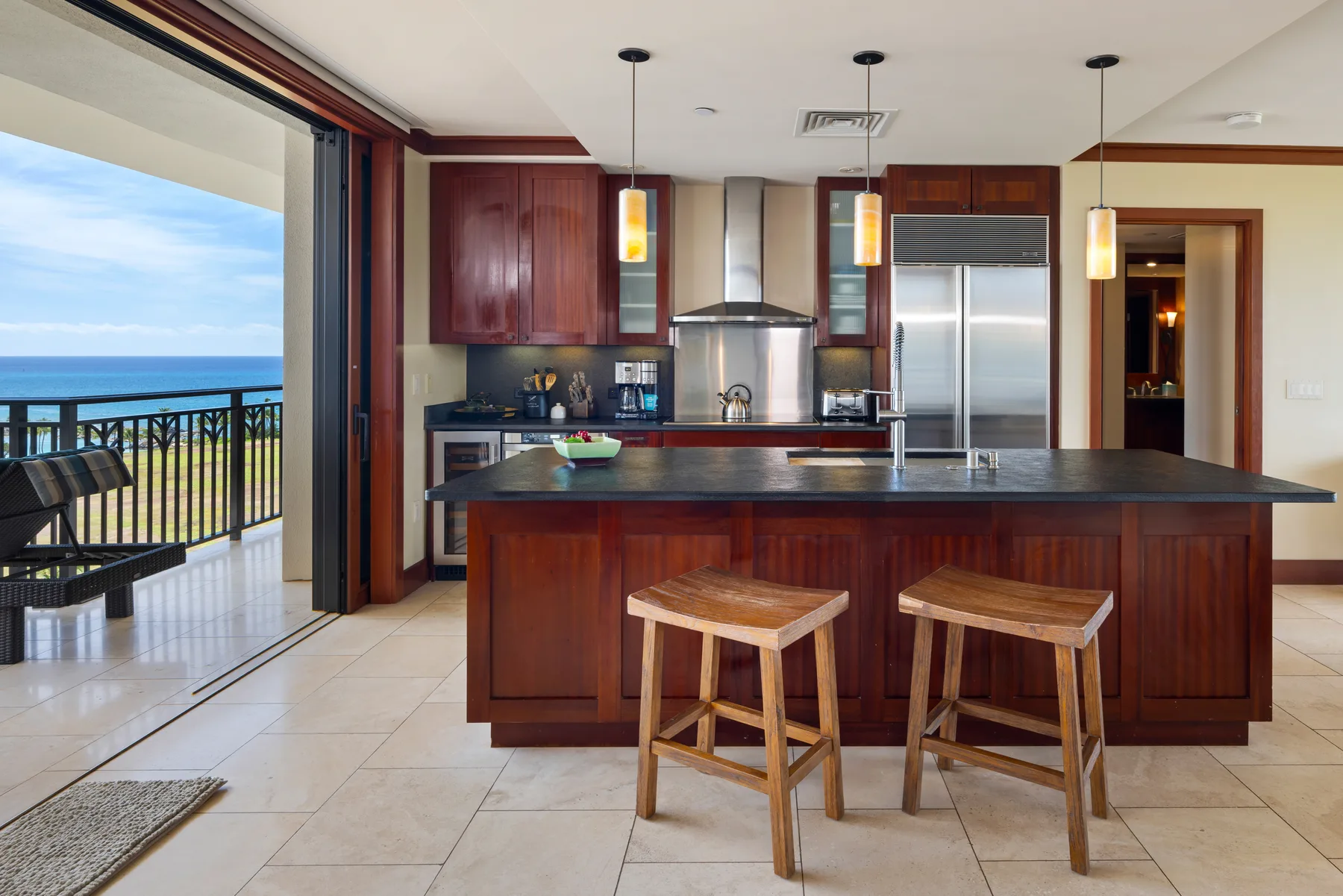 Una cocina moderna cuenta con una isla amplia, dos taburetes de madera y electrodomésticos de acero inoxidable.