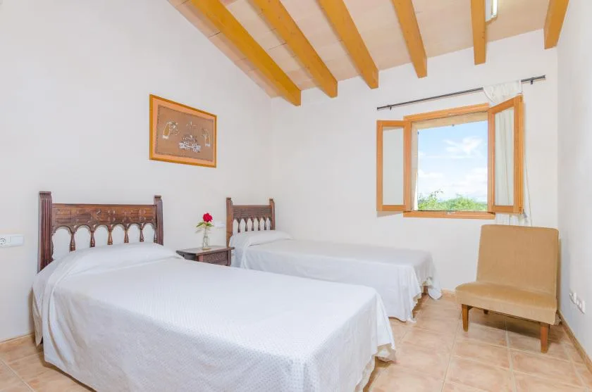 Un dormitorio luminoso con dos camas y una ventana abierta con vistas a la vegetación.