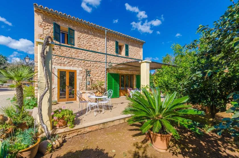 Una casa de piedra con una zona de estar en el patio y plantas frondosas.