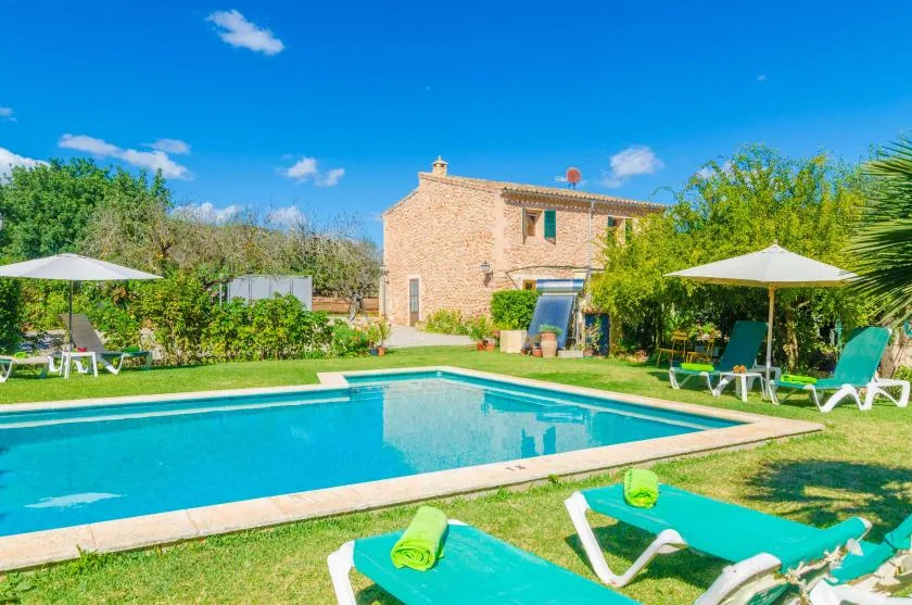 Una piscina está frente a una casa de piedra, con tumbonas sobre el césped.