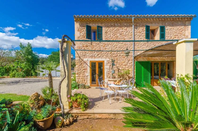 Una casa de piedra con contraventanas verdes da a un patio con asientos al aire libre.