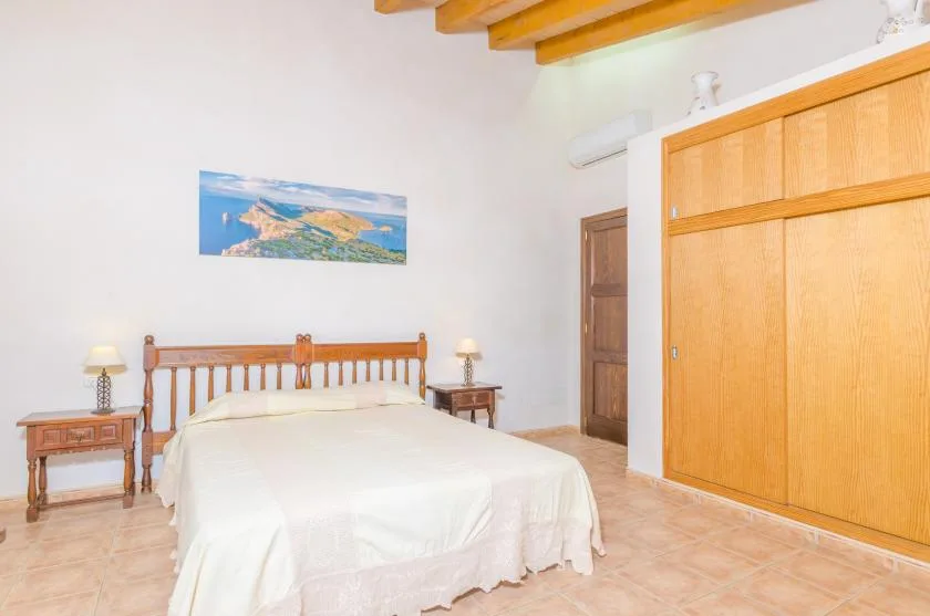 Un dormitorio con una cama doble, un armario de madera y vigas a la vista en el techo.