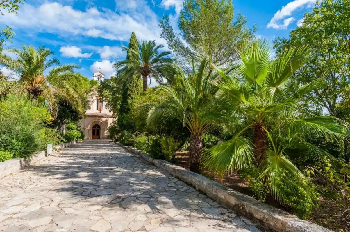 Un sendero de piedra atraviesa un jardín frondoso hacia un pequeño edificio.