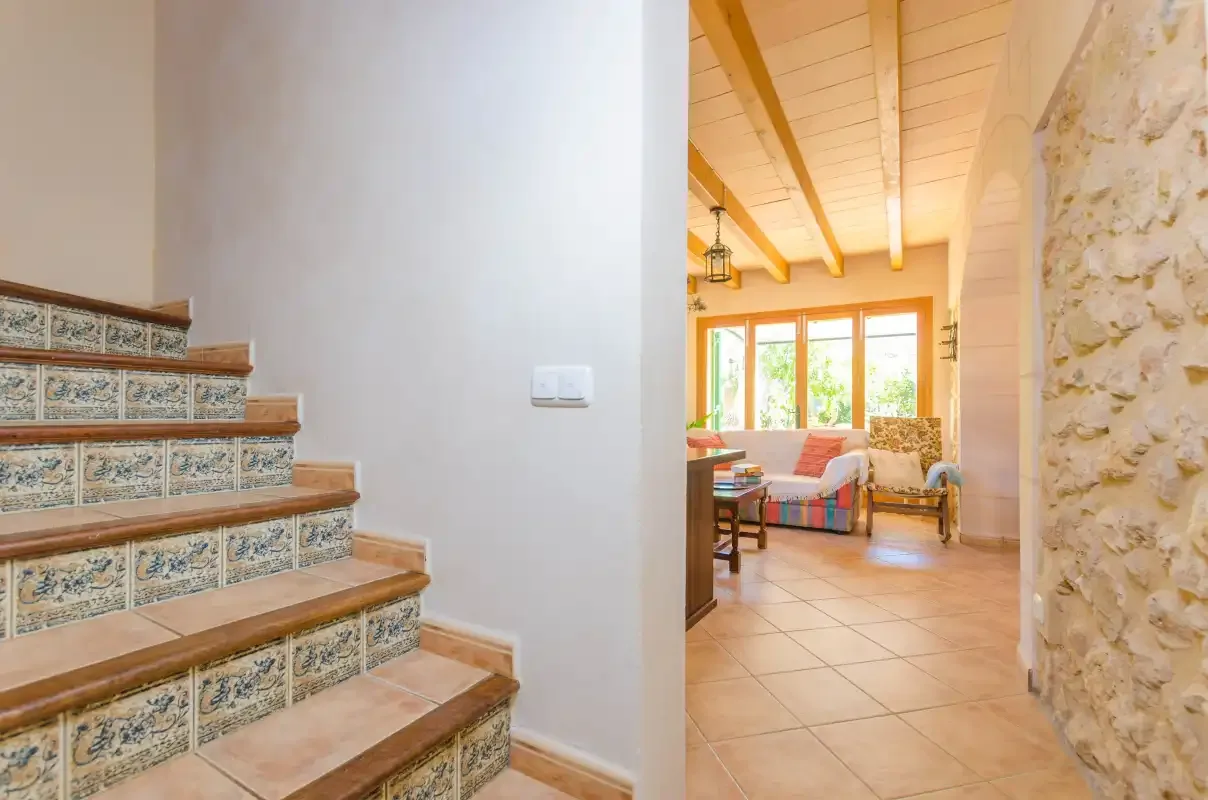 Una escalera alicatada da a una habitación luminosa con asientos y grandes ventanas.