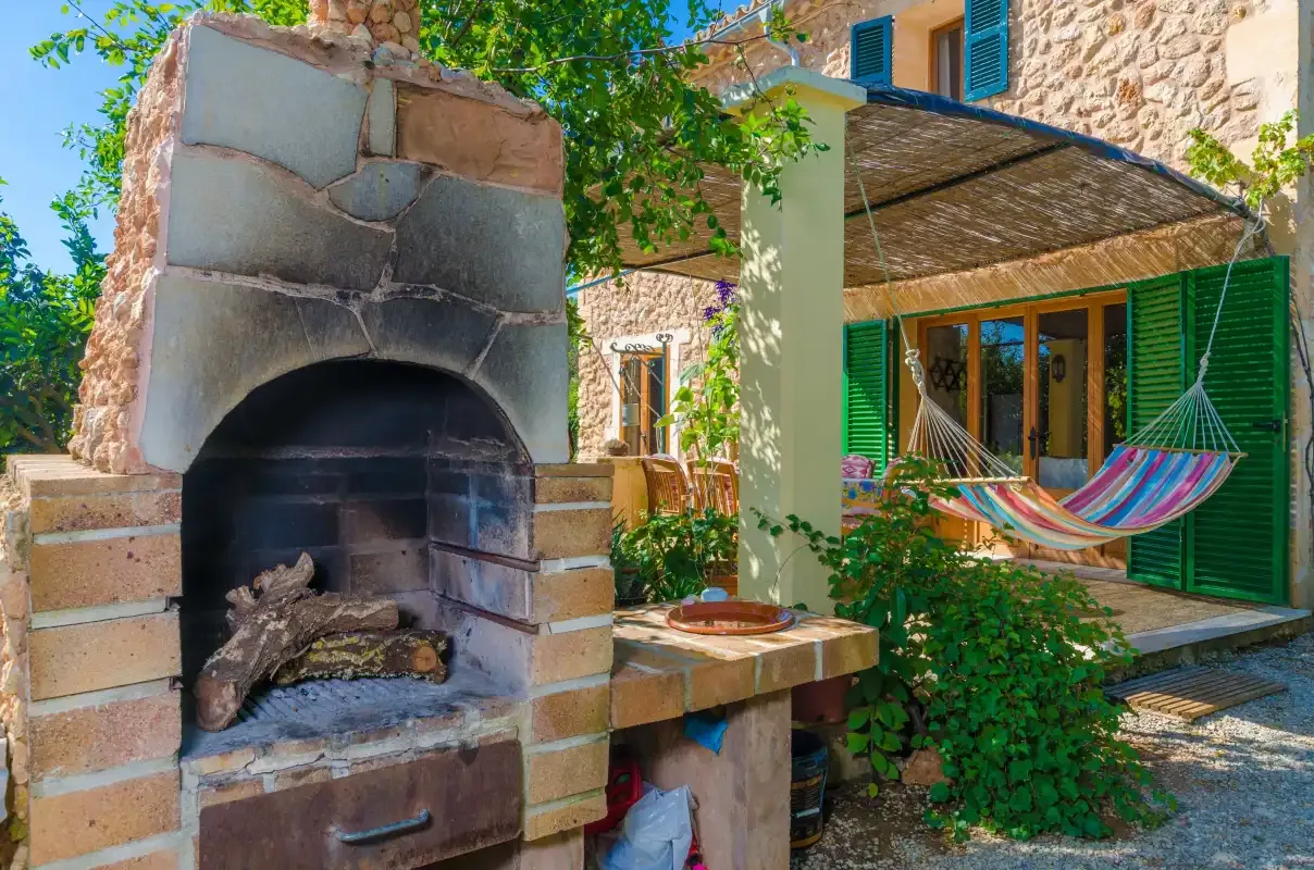 Un patio de piedra tiene una chimenea exterior y una hamaca colorida bajo una zona sombreada.