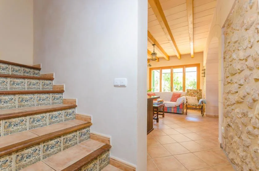Una escalera con azulejos da a una luminosa sala de estar con vigas expuestas.