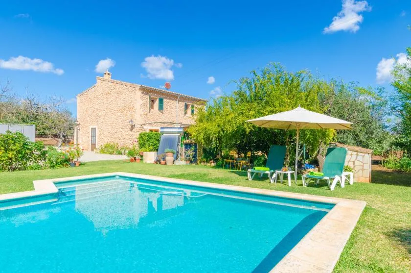 Una piscina junto a una casa de piedra, con asientos a la sombra de una sombrilla.