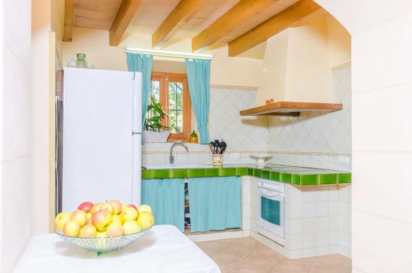 Una cocina luminosa con cortinas turquesas, encimeras verdes y vigas de madera en el techo.