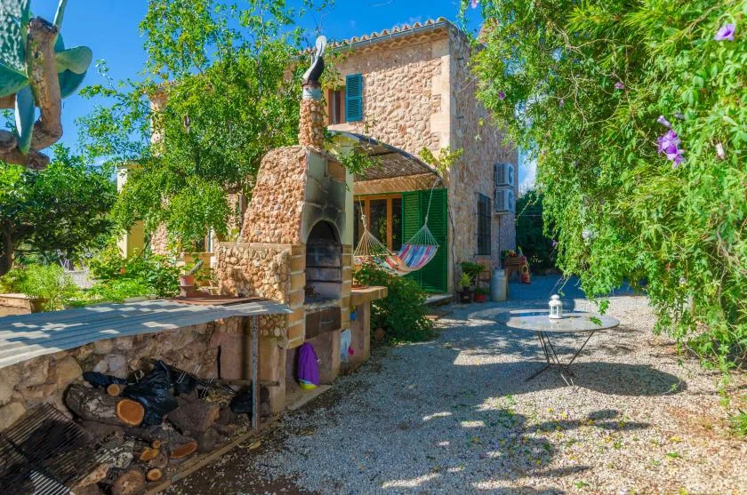 Un patio de piedra con una barbacoa empotrada, una hamaca y vegetación alrededor.
