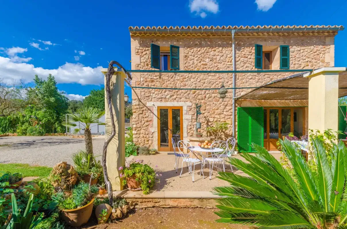 Una casa de piedra con patio pavimentado, asientos al aire libre y plantas alrededor.