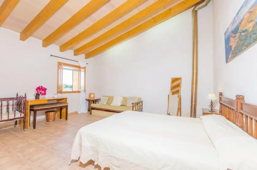 Un dormitorio luminoso con una cama grande, una zona de estar y vigas a la vista.