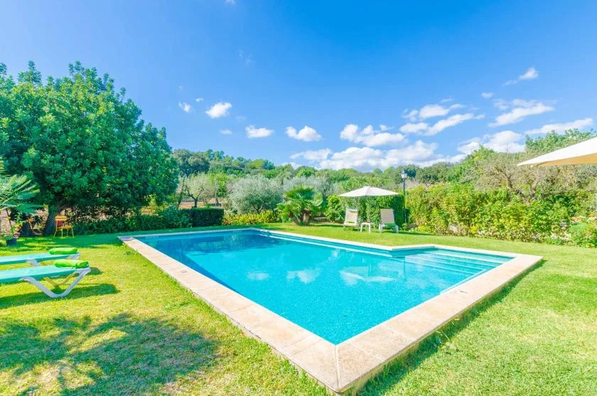Una piscina al aire libre está en un jardín con césped bajo un cielo azul.