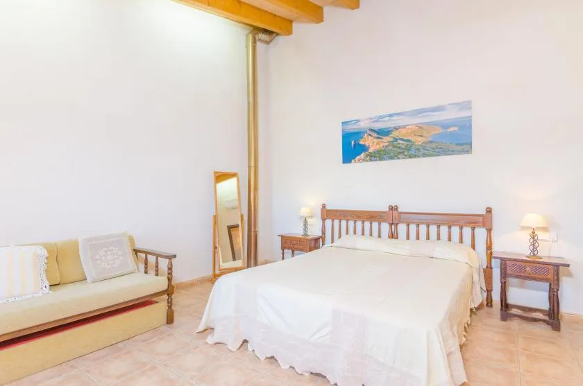 Un dormitorio con una cama, un sofá y un cuadro de paisaje en la pared.
