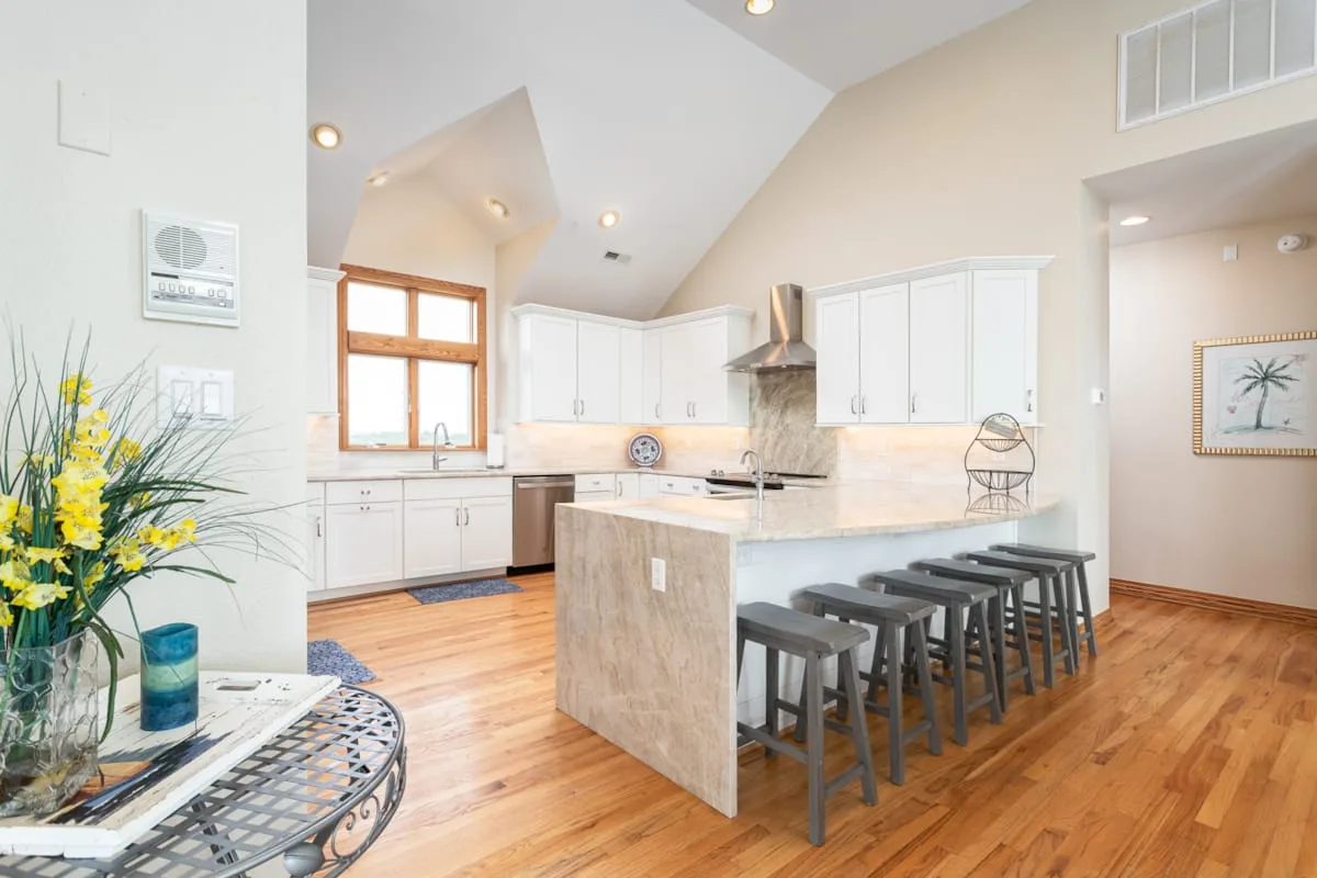 A bright kitchen has white cabinets, a central island, and wood flooring.