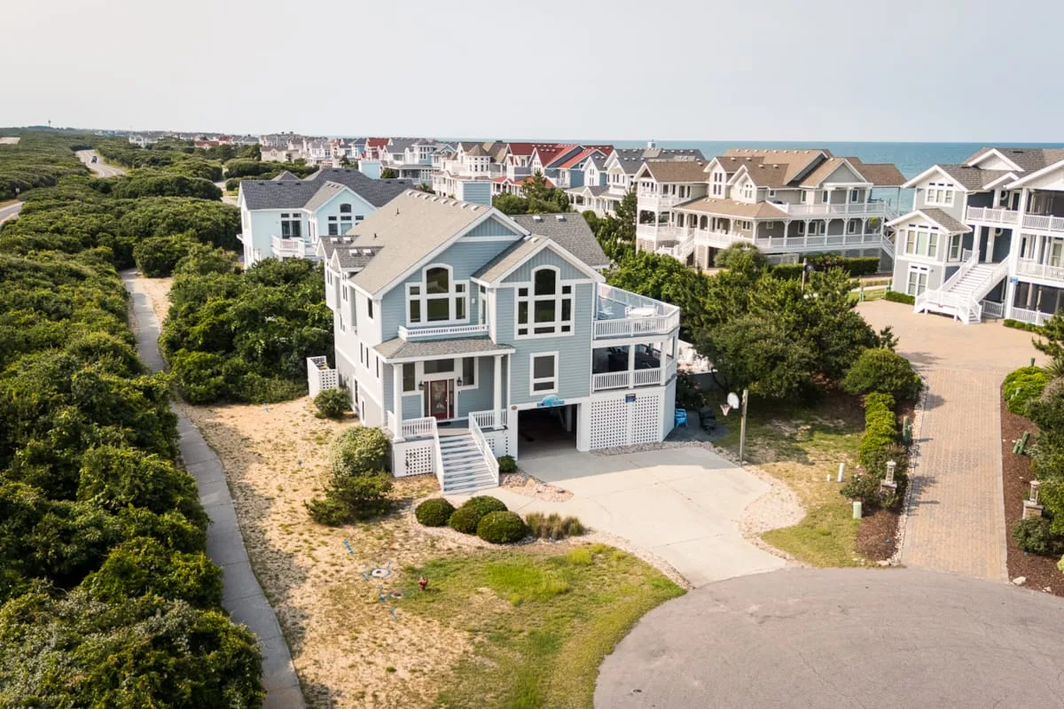 Aerial view of coastal houses surrounded by greenery and sandy paths.