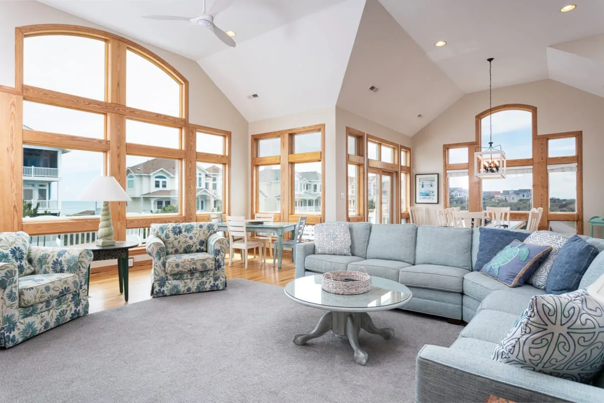 A bright living room has large wood-framed windows and a seating area around a coffee table.