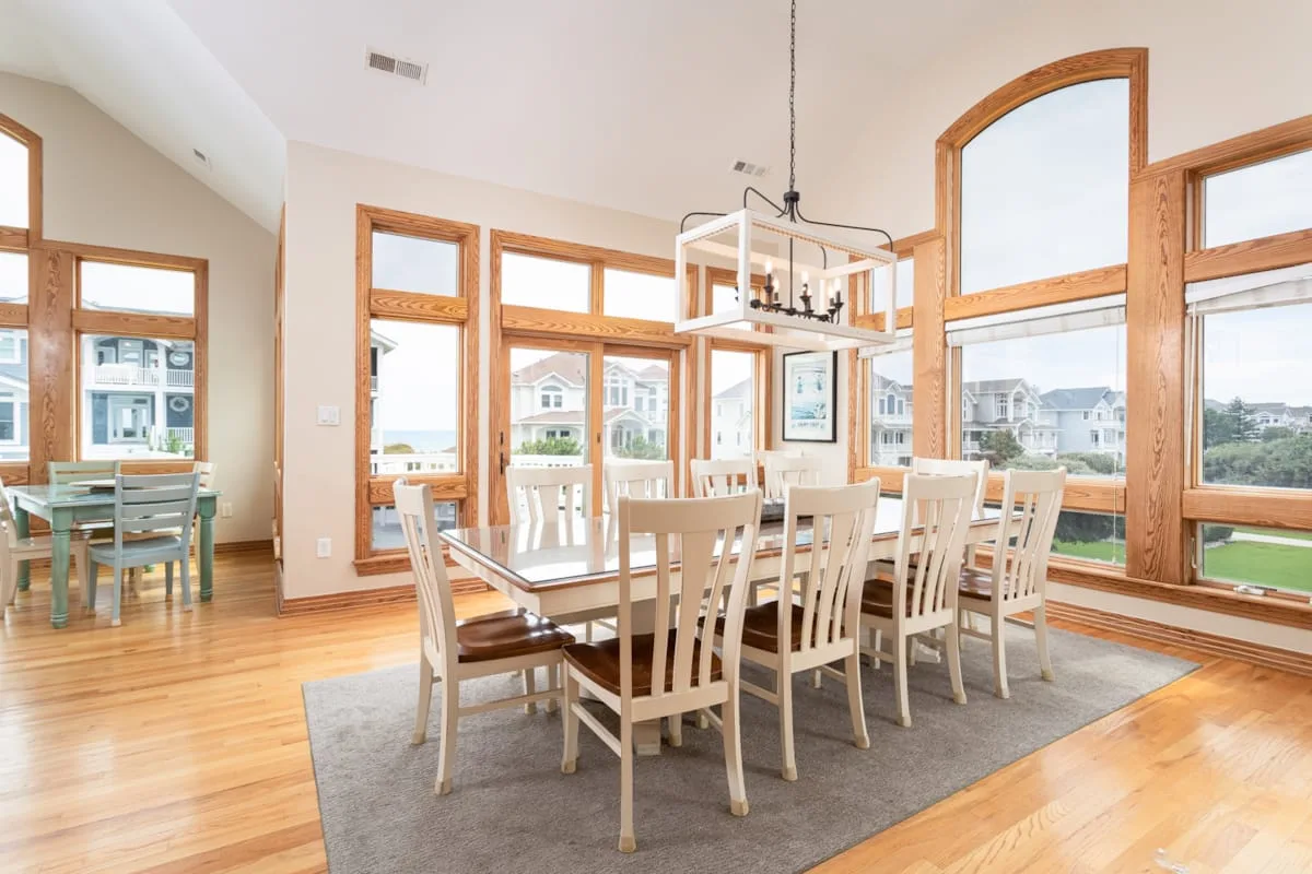 A bright dining room with a long table beside large windows.